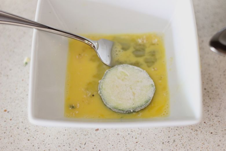 Flour coated zucchini slice in the beaten egg bowl.  