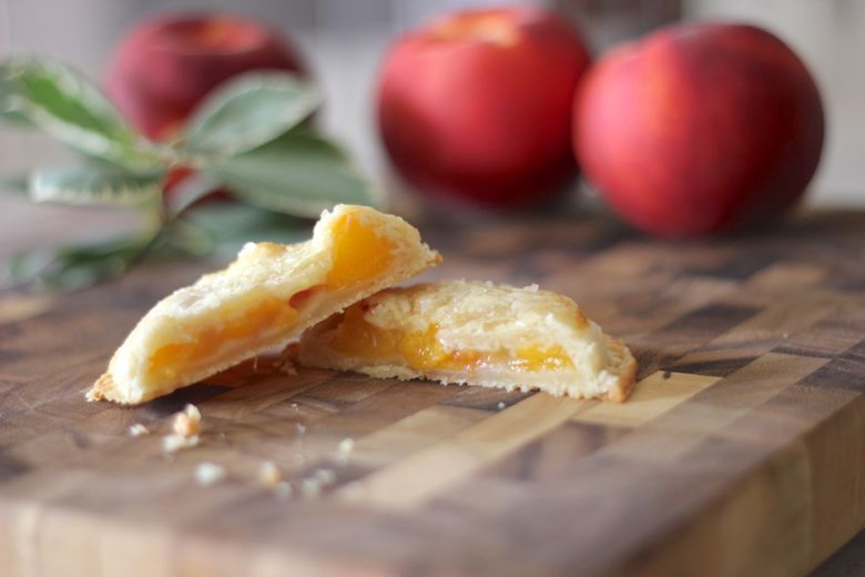 Peach Hand Pie cut in half on a cutting board with whole peaches in the background.  