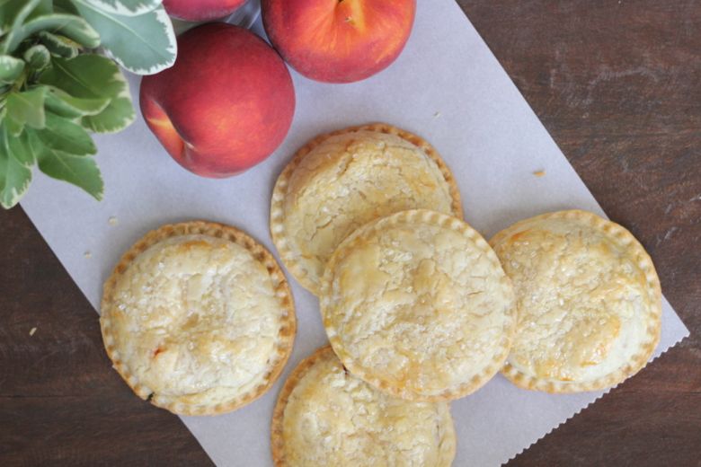 Peach Hand Pies on parchment paper next to whole peaches.  