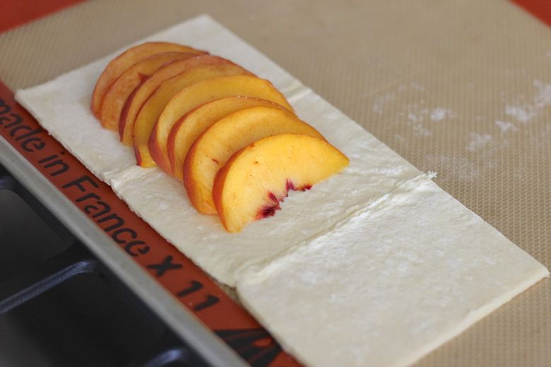 Peach slices arranged on puff pastry on Silpat lined baking sheet.  