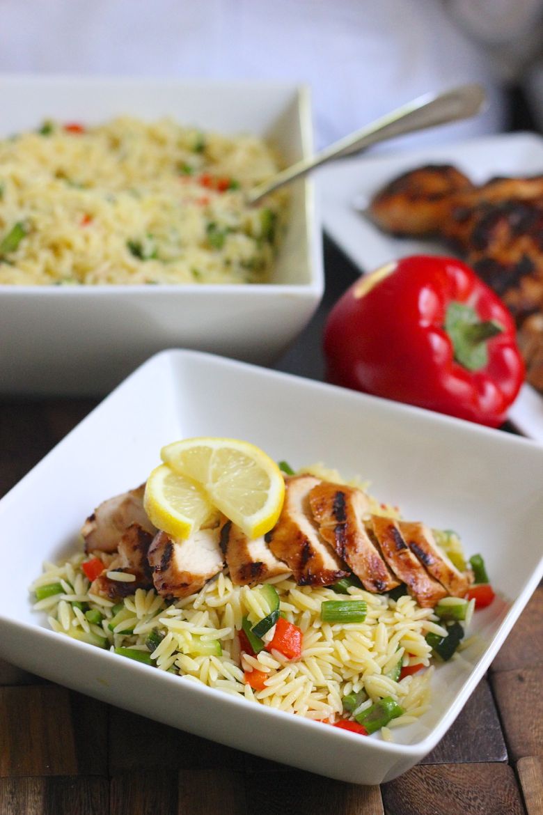 Lemon Garlic Orzo With Roasted Vegetables and sliced grilled chicken on top in a bowl.  