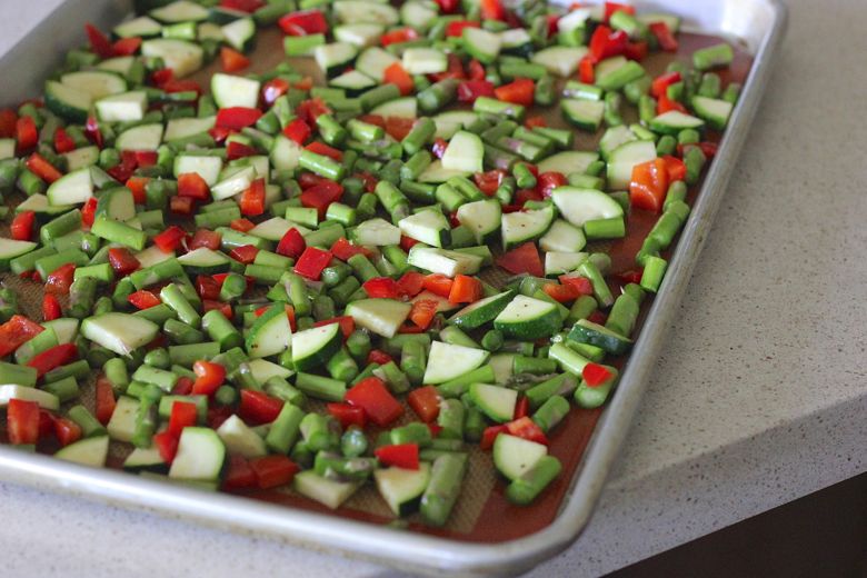 Chopped zucchini, red peppers and asparagus on a baking sheet.  