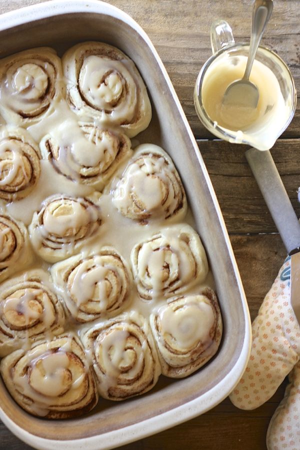 Maple Glazed Cinnamon Rolls in a baking dish with a cup of the maple glaze next to it.  