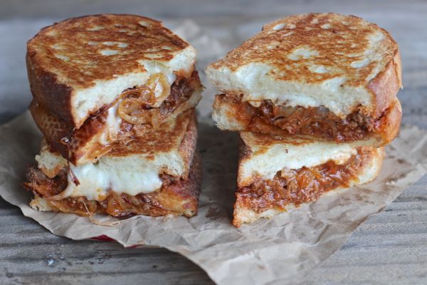 Two Sloppy Joe Paninis With Baby Swiss and Caramelized Onions cut in half and stacked next to each other.  