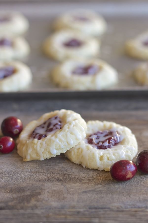 Two Cranberry Thumbprint Cookies With Almond Glaze on a board with cranberries.