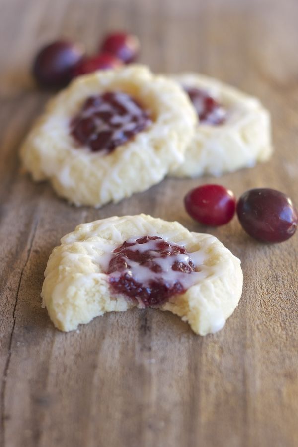 Three Cranberry Thumbprint Cookies With Almond Glaze on a board with cranberries and a bite taken out of one cookie.  