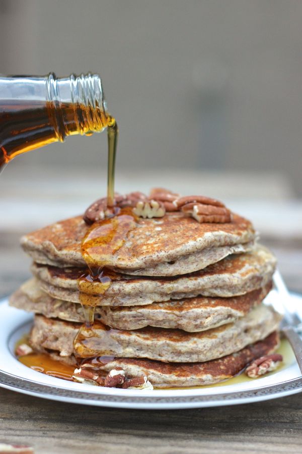 Healthy Pumpkin Pie Spice Oatmeal Flax Pancakes stacked and topped with pecans and maple syrup being poured over it.    