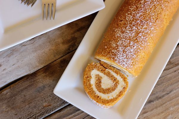 Pumpkin Roll With Maple Cream Cheese Filling on a serving plate with one piece sliced off the end.  