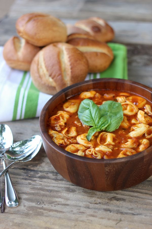 Easy Tomato Basil Soup With Chicken Sausage and Cheese Tortellini in a bowl with garnish on top and dinner rolls in the background.  