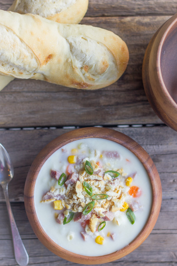 Creamy Potato Soup With Ham in a bowl with loaves of bread next to it. 
