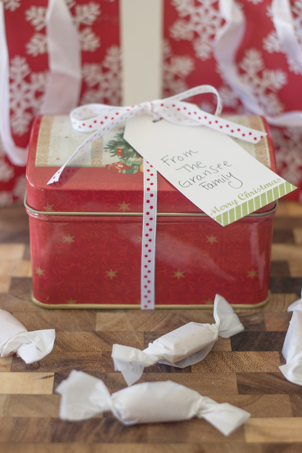 Homemade Soft Caramels wrapped in parchment paper in front of a Christmas tin.  