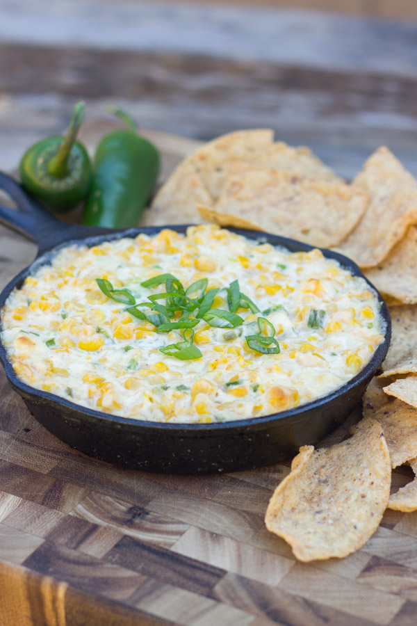 Hot Jalapeño Corn Dip in a cast iron skillet with jalapeños and tortilla chips around it.  