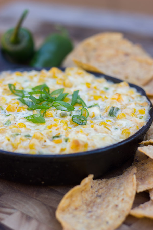 Hot Jalapeño Corn Dip in a cast iron skillet with jalapeños and tortilla chips around it.