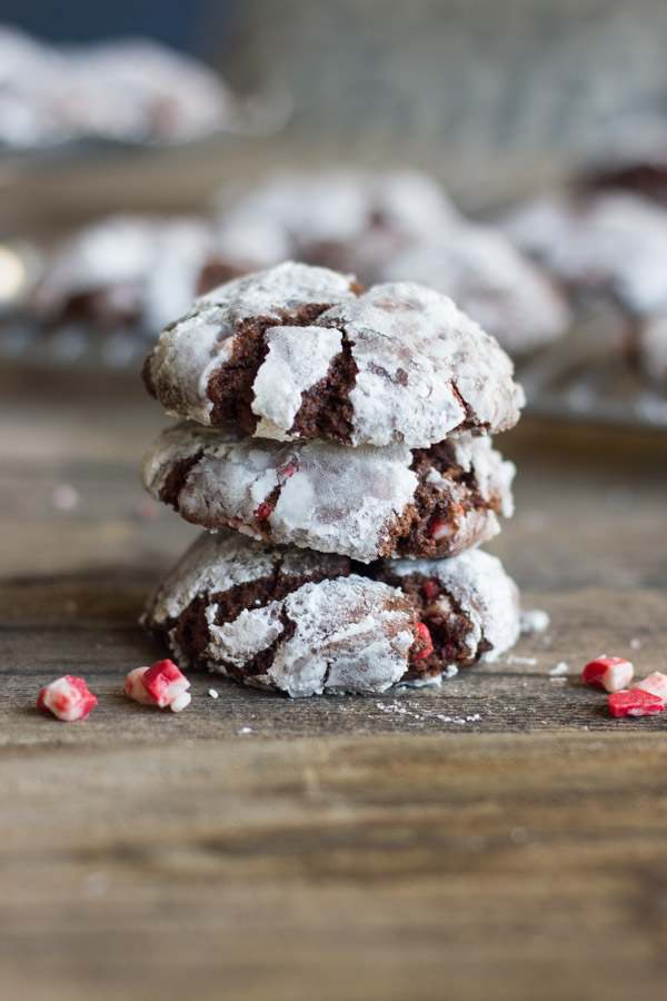 Peppermint Crunch Chocolate Crinkle Cookies stacked in a pile of three with bits of peppermint next to it.  