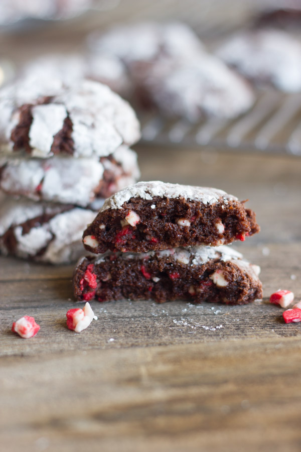 Peppermint Crunch Chocolate Crinkle Cookie cut in half and stacked with bits of peppermint next to it on a board.  
