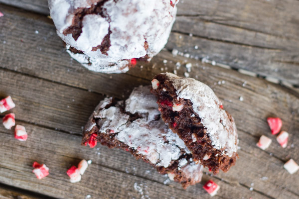 Peppermint Crunch Chocolate Crinkle Cookie cut in half with bits of peppermint next to it on a board.  