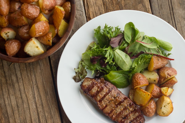 Roasted Red Potatoes on a dinner plate with steak and salad, next to a serving bowl with Roasted Red Potatoes in it.  