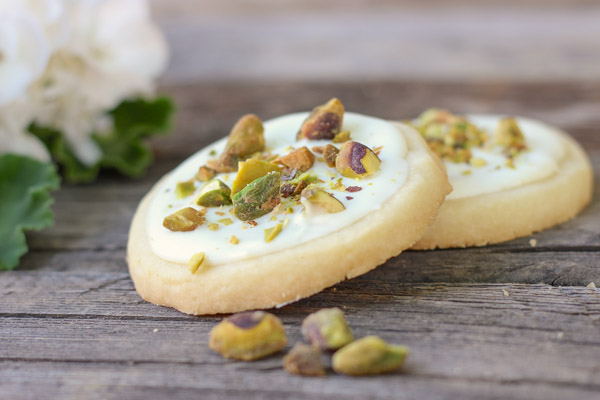 Two White Chocolate Pistachio Shortbread Cookies on a board with a few pistachios.  