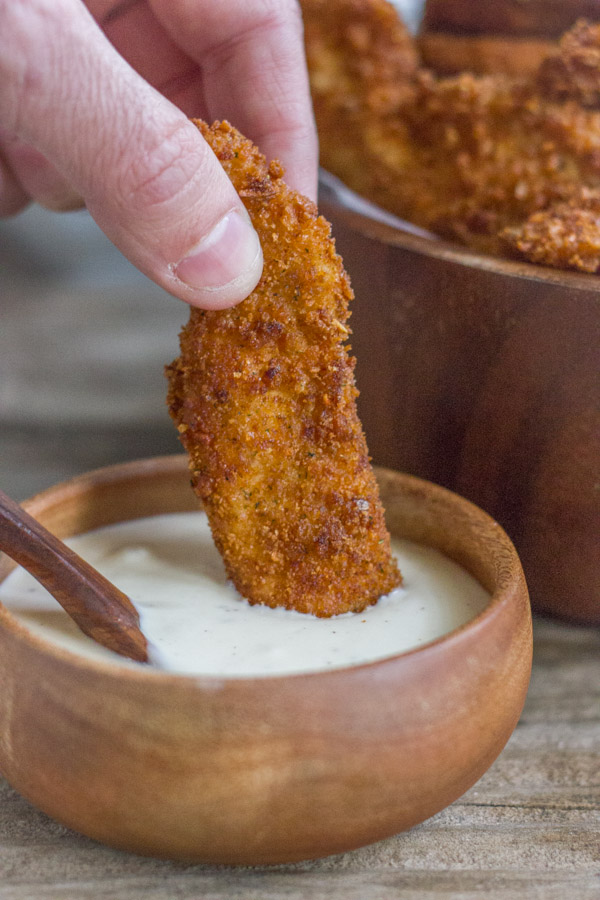 Extra Crispy Chicken Strip being dipped into a small bowl of dipping sauce.  