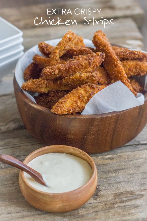 Extra Crispy Chicken Strips piled into a large bowl, with a small bowl of dipping sauce next to it.  