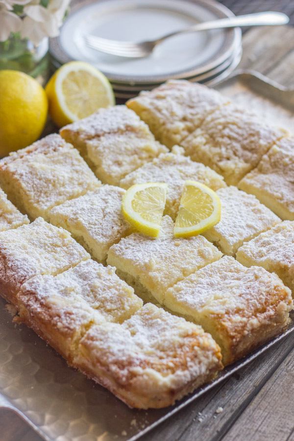 Greek Yogurt Cream Cheese Lemon Coffee Cake cut in squares on a serving tray with two slices of lemon on top for garnish.  