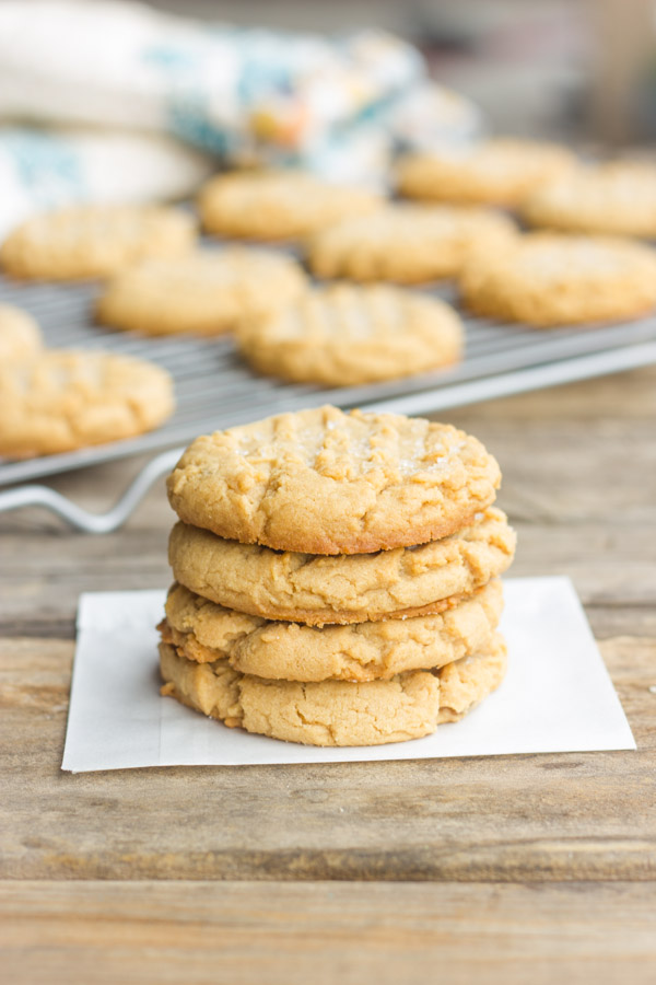 Brown Butter Peanut Butter Cookies stacked in a pile of four with more cookies on a cooling rack in the background.  
