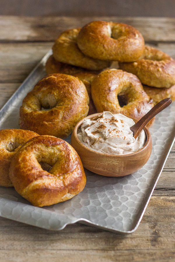 Whole Wheat Soft Pretzel Bagels stacked on a serving platter with a small bowl of Cinnamon Sugar Cream Cheese.