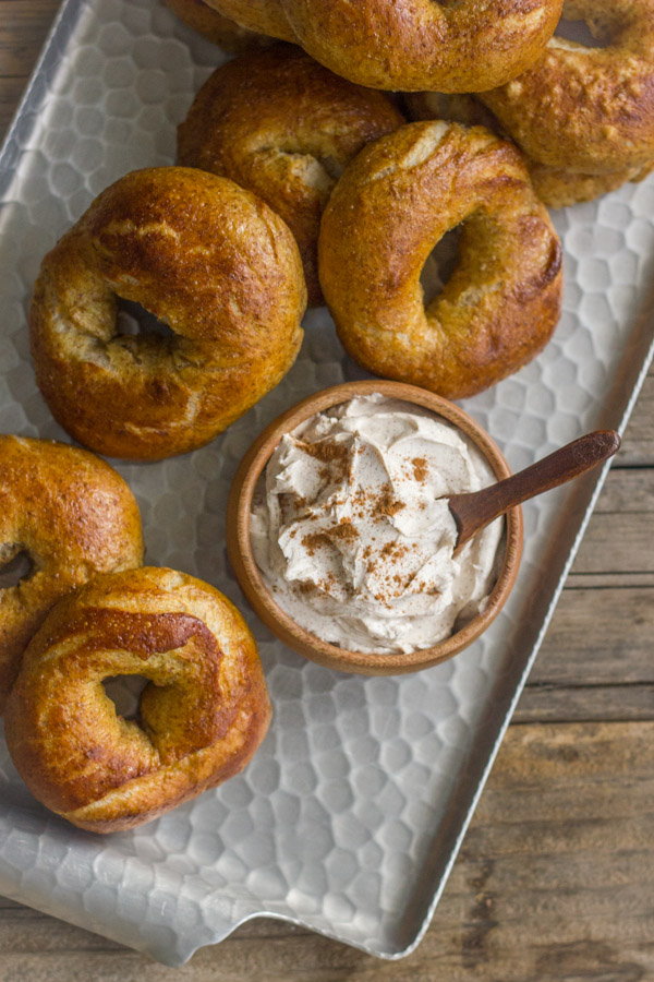 Whole Wheat Soft Pretzel Bagels stacked on a serving platter with a small bowl of Cinnamon Sugar Cream Cheese.