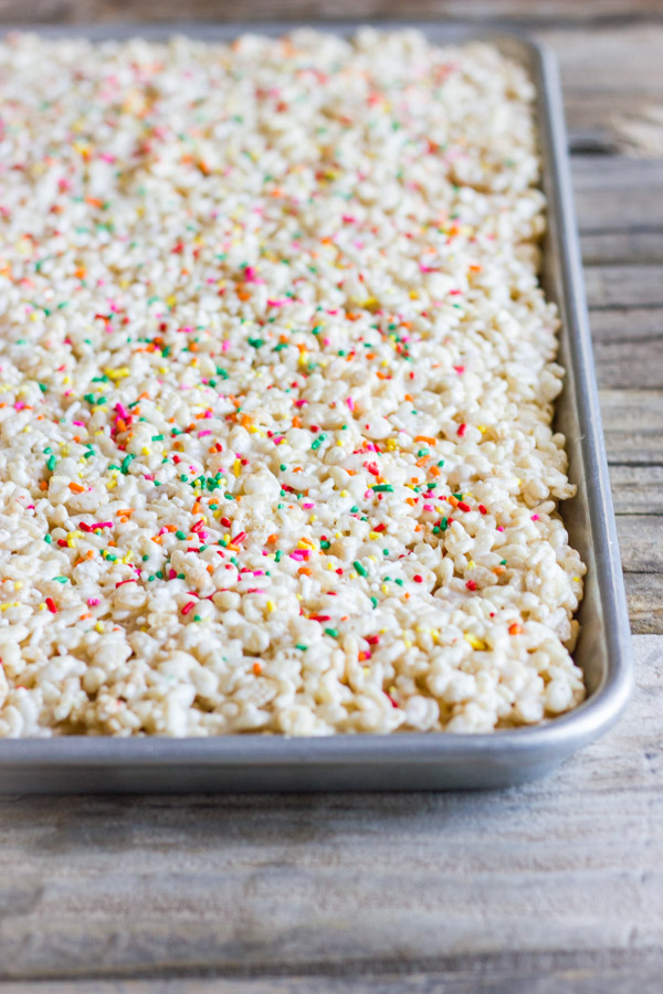 Coconut Oil Rice Krispie Treats spread out on a baking sheet and topped with sprinkles.    