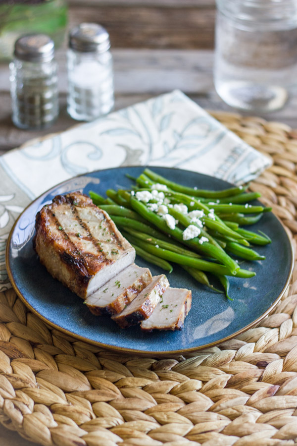 Marinated Grilled Pork Chop on a plate with green beans topped with feta.  