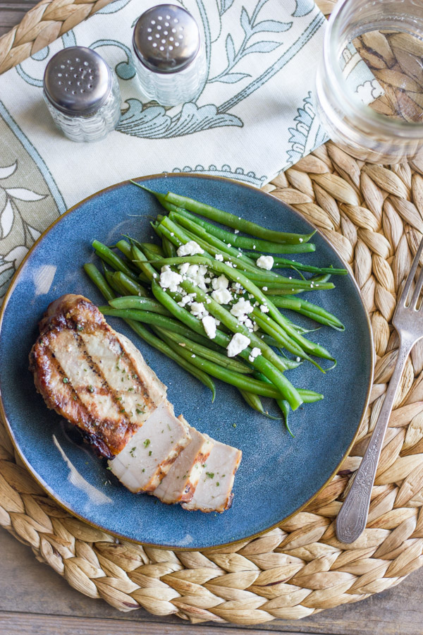 Marinated Grilled Pork Chop on a plate with green beans topped with feta.  