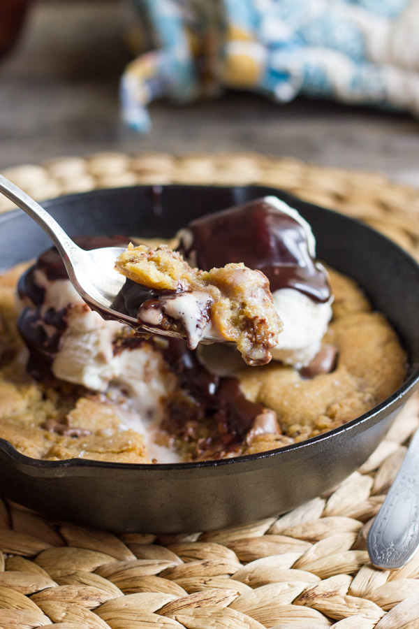 Salted Rolo Chip Pizookie in a small cast iron skillet, topped with vanilla ice cream and Homemade Hot Fudge, and a spoon with a bite full on it.  