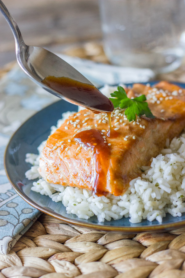 Teriyaki Glazed Salmon served on top of a bed of white rice, with a spoon drizzling the teriyaki glaze on top of the salmon. 