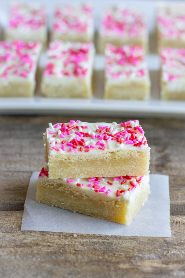 Two Easy White Chocolate Sugar Cookie Bars stacked on top of each other, with more bars in the background on a serving platter.  
