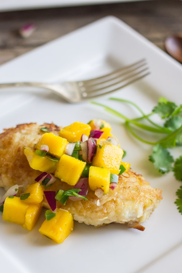 Coconut Crusted Chicken With Mango Salsa on top, on a plate with a fork and cilantro.