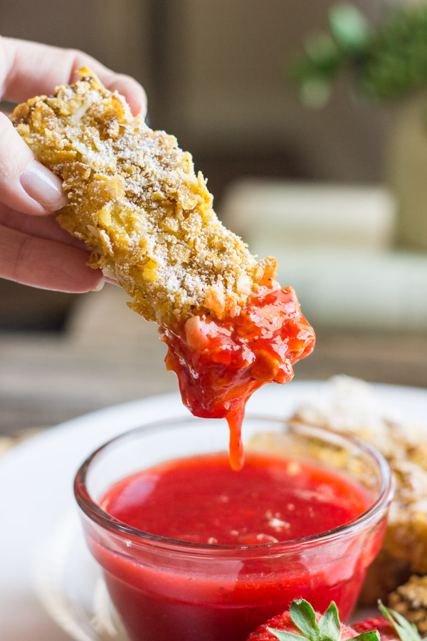 Crunchy Baked French Toast Stick being dipped into a glass dish of Strawberry Syrup.  