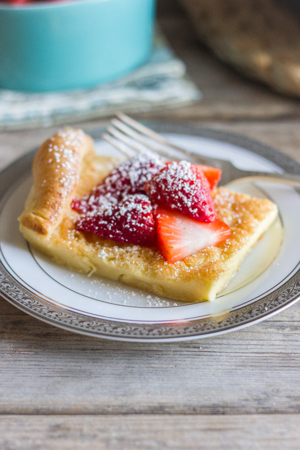 Dutch Baby Pancake slice on a plate topped with strawberries and powdered sugar.  