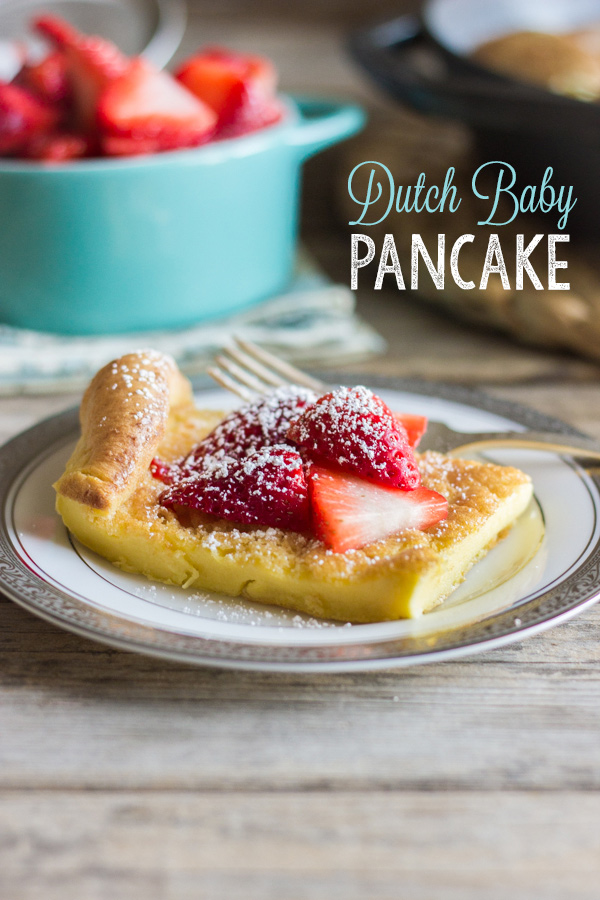 Dutch Baby Pancake slice on a plate topped with strawberries and powdered sugar, with a bowl of strawberries in the background.  