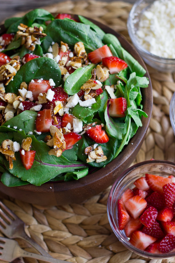 Strawberry and Spinach Salad with Almond Vinaigrette in a bowl, with a small glass dish of strawberries and a small glass dish of Feta cheese next to it.  
