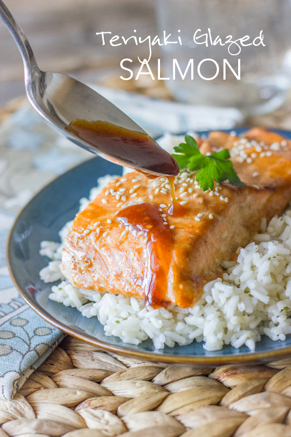 Teriyaki Glazed Salmon served on top of a bed of white rice, with a spoon drizzling the teriyaki glaze on top of the salmon. 