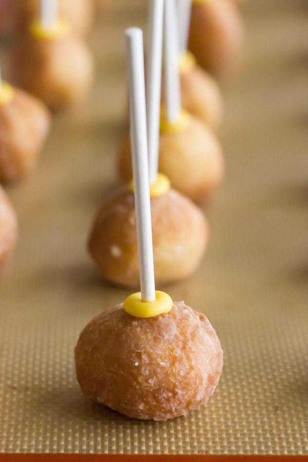 Donut holes with lollipop sticks pressed into them, on a Silpat lined baking sheet.