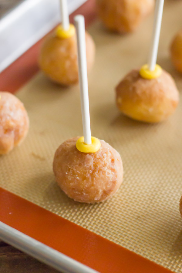 Donut holes with lollipop sticks pressed into them, on a Silpat lined baking sheet.