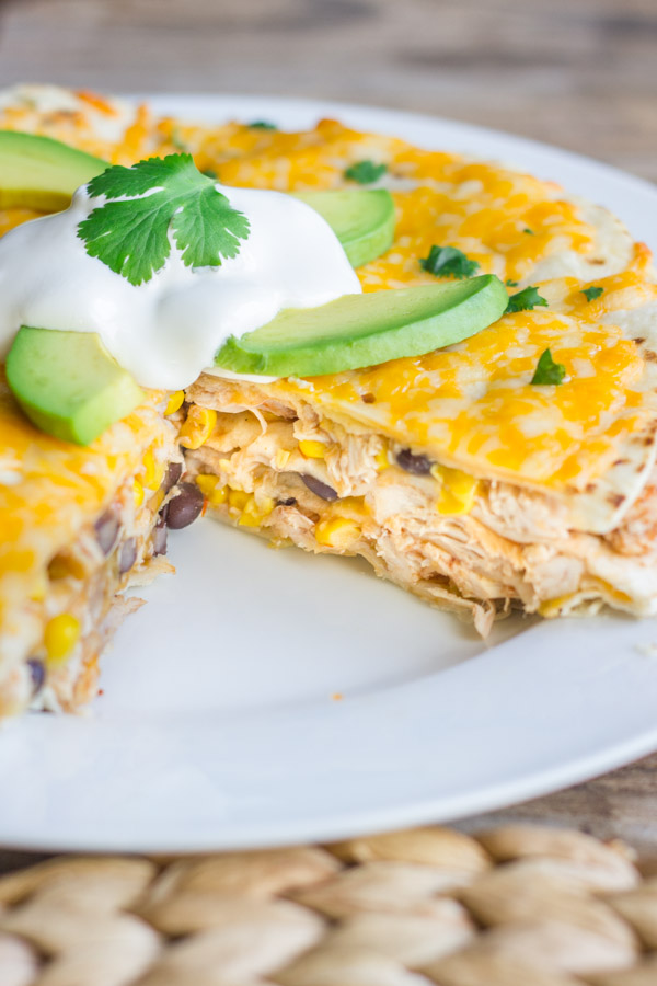 Southwestern Chicken Taco Pie on a large plate, topped with sour cream, avocado slices and cilantro, with a slice missing.   
