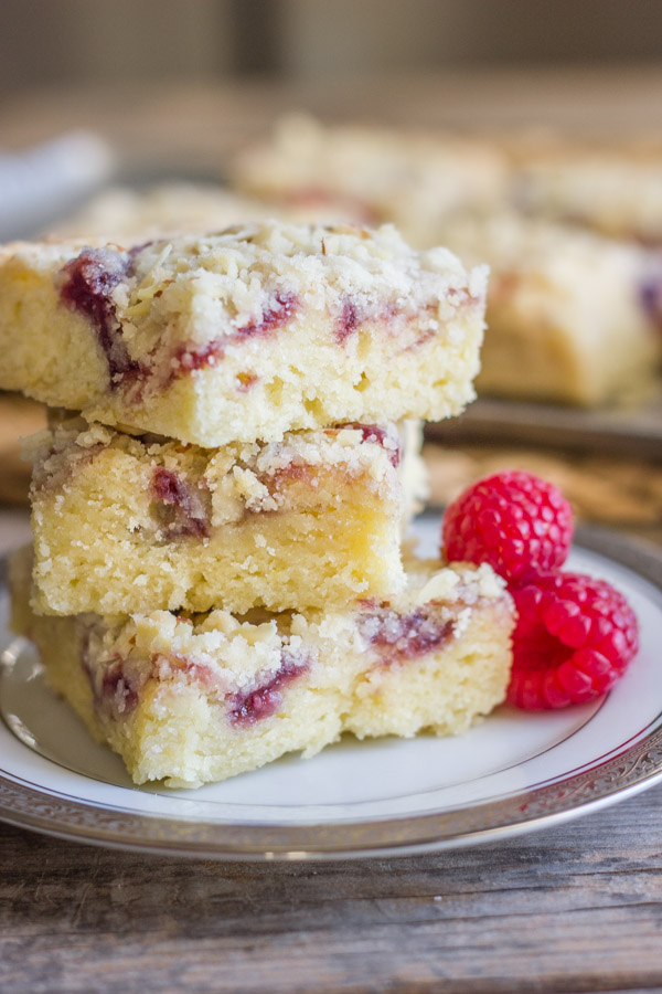 Raspberry Almond Crumb Bar squares stacked in a pile of three on a plate with fresh raspberries next to it.  
