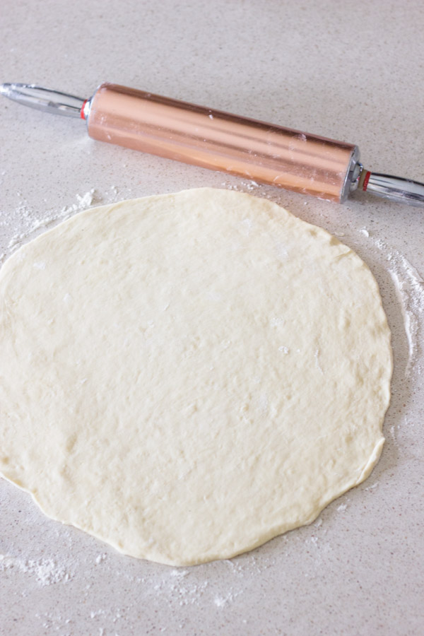 The Best Butterhorn Rolls dough rolled out into a circle, with a rolling pin next to it.  