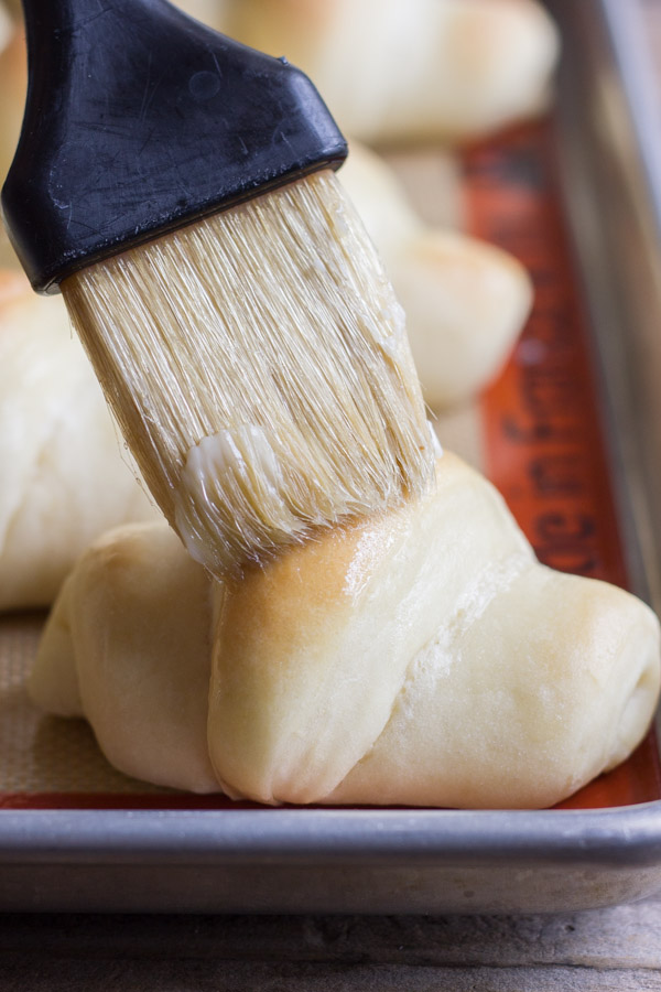 A Butterhorn roll on a baking sheet being brushed with butter. 