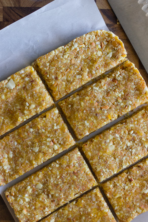 No Bake Apricot Almond Bars on parchment paper on top of a cutting bard with a knife.  