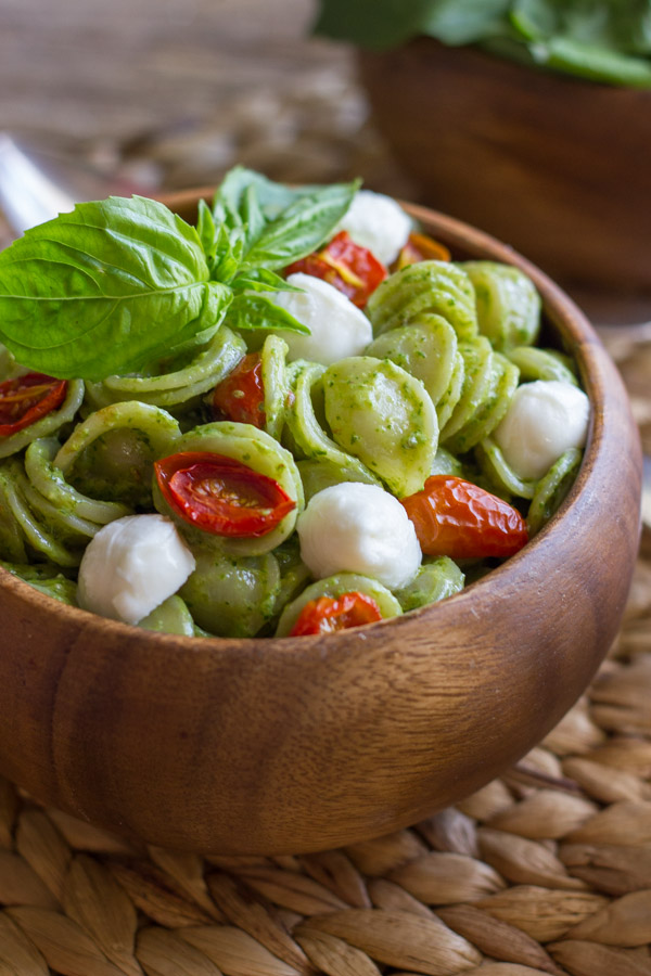 Orecchiette With Pesto and Oven Roasted Tomatoes in a bowl, topped with fresh basil leaves.  