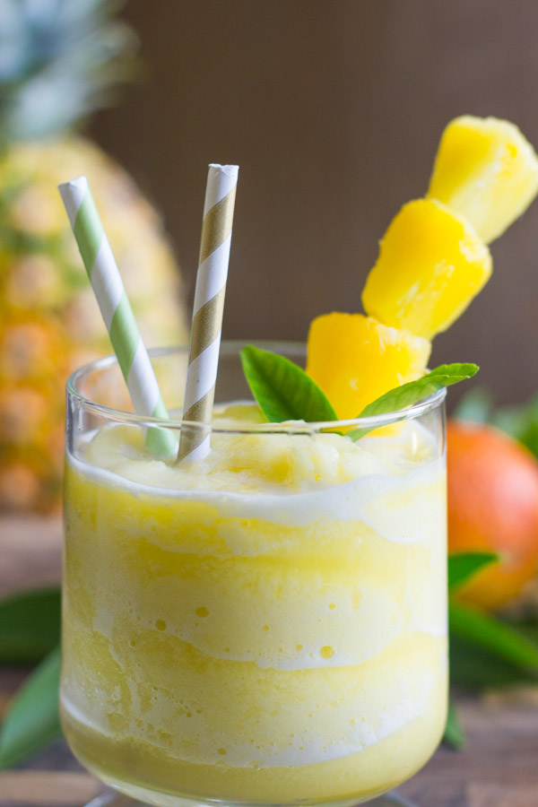 Skinny Pineapple Orange Slush in a glass with two straws and pineapple chunks on a stick.