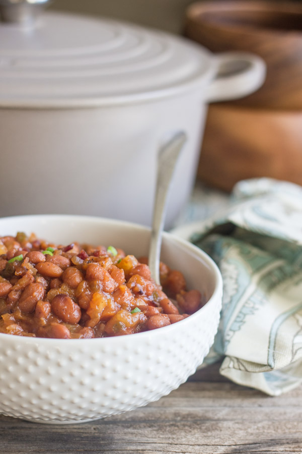 Sweet And Spicy BBQ Baked Beans in a bowl with a spoon in it and a Le Creuset French Oven in the background.  